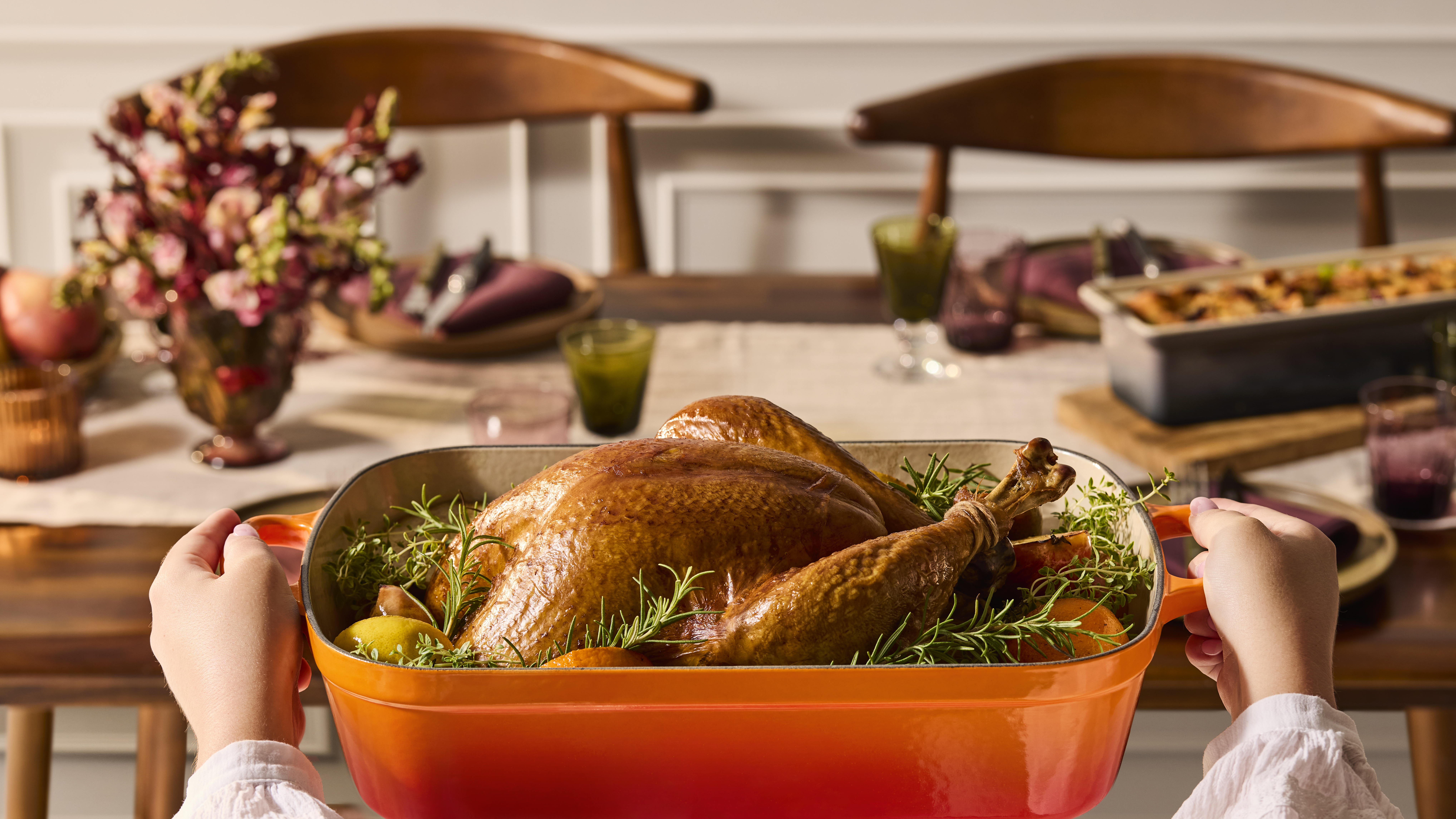 Person holding a Le Creuset Cast Iron Signature Roasting Tray in Flame with roasted chicken